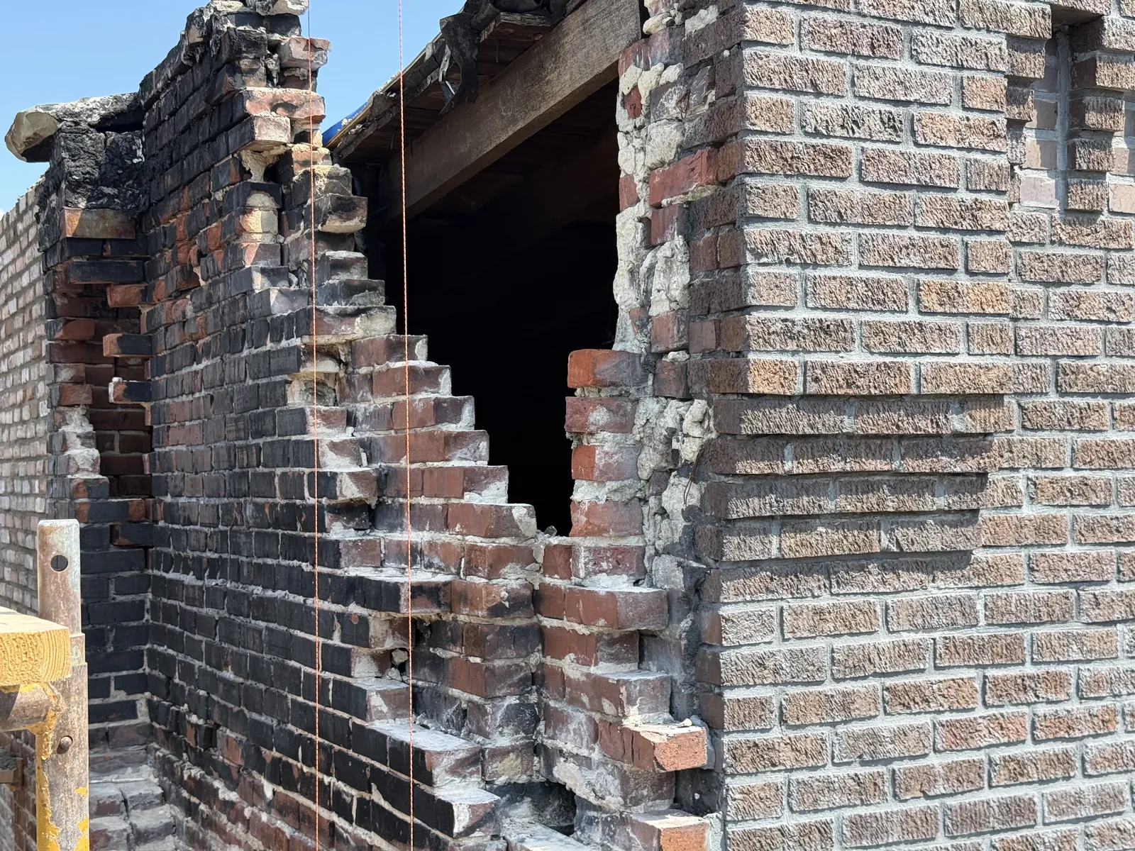 A damaged section of an older brick wall cut back in steps so new brick can be toothed into the sound wall
