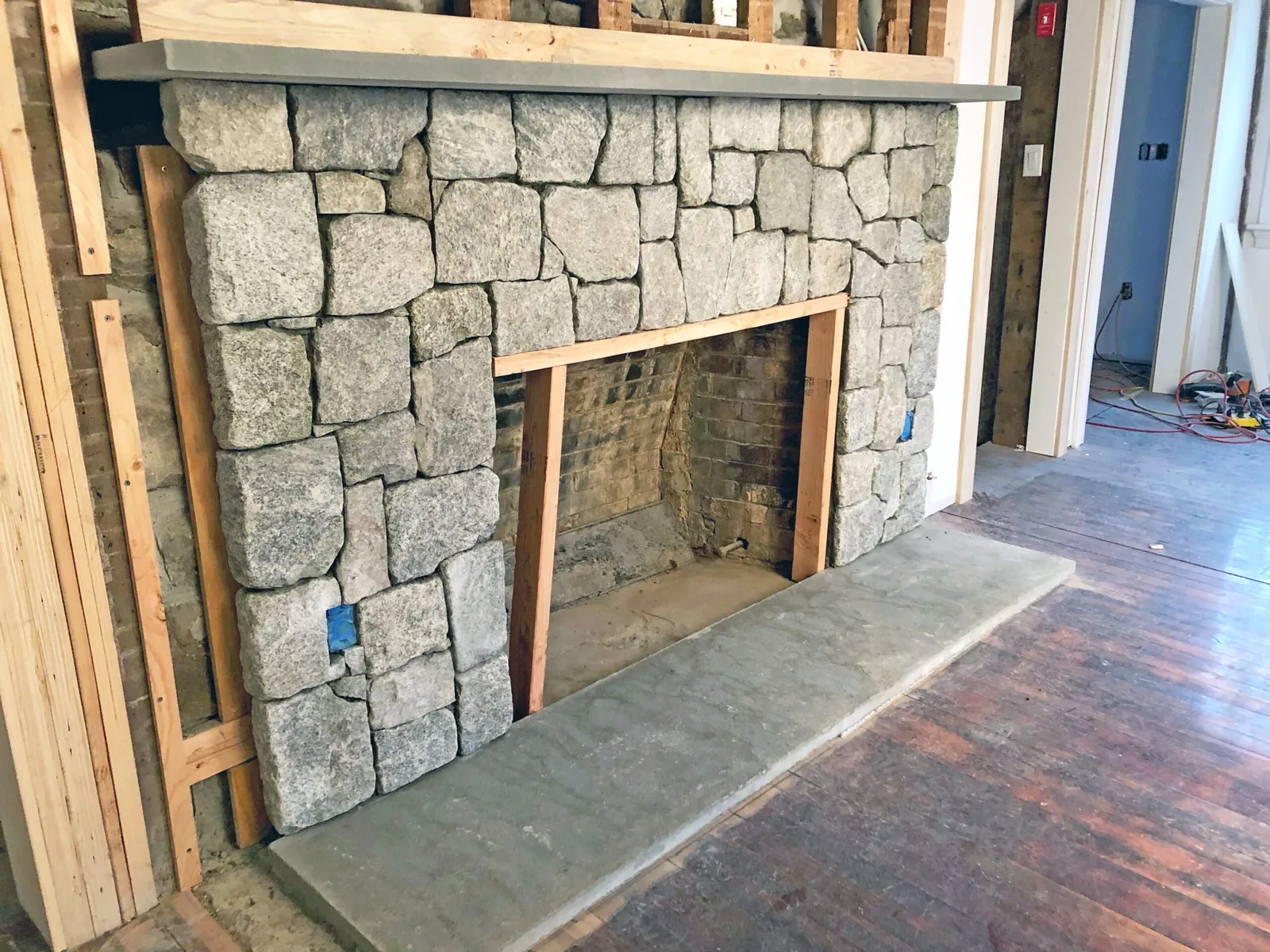 Fireplace remodel in progress with a natural stone veneer face, a stone hearth and new framing around the firebox