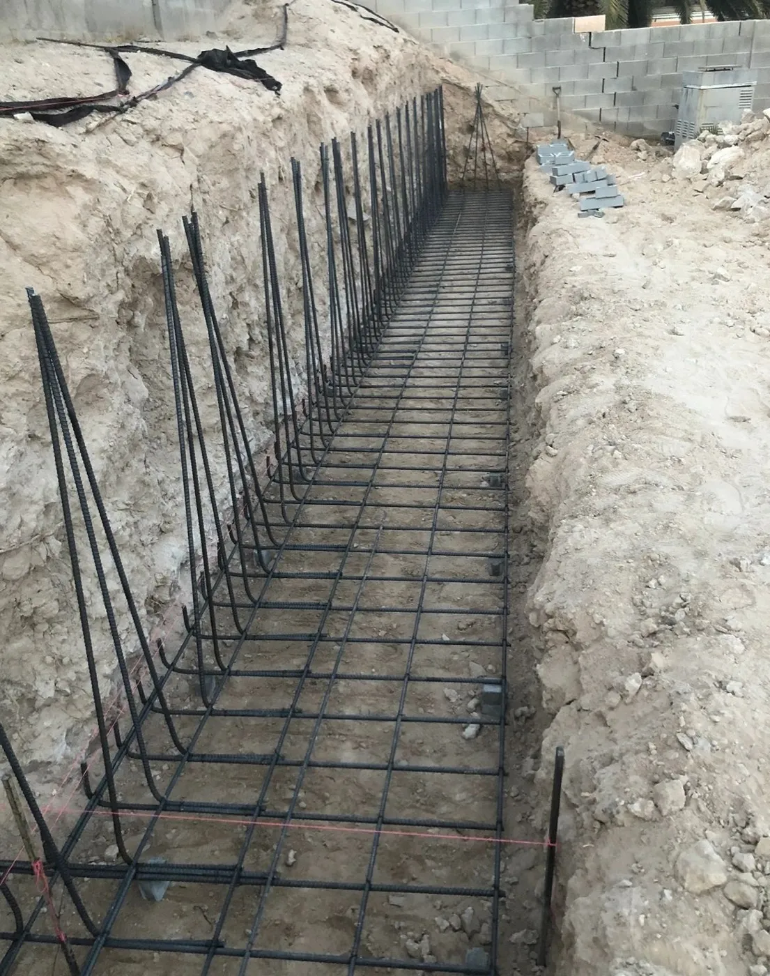 Rebar cage tied in a footing trench cut through caliche on a Las Vegas lot before the pour