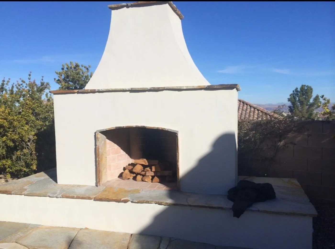 Stucco outdoor fireplace with a wood mantel shelf